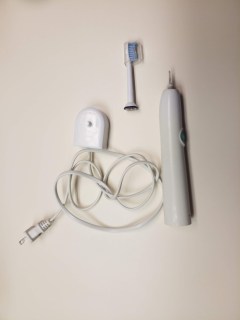 Sonicare electric toothbrush charging base, handle, and a toothbrush head with plastic cover.
